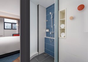 Ein modernes Hotelzimmer mit Dusche, einem Bett, einem Fenster und einem Ablagefächer mit Handtüchern.