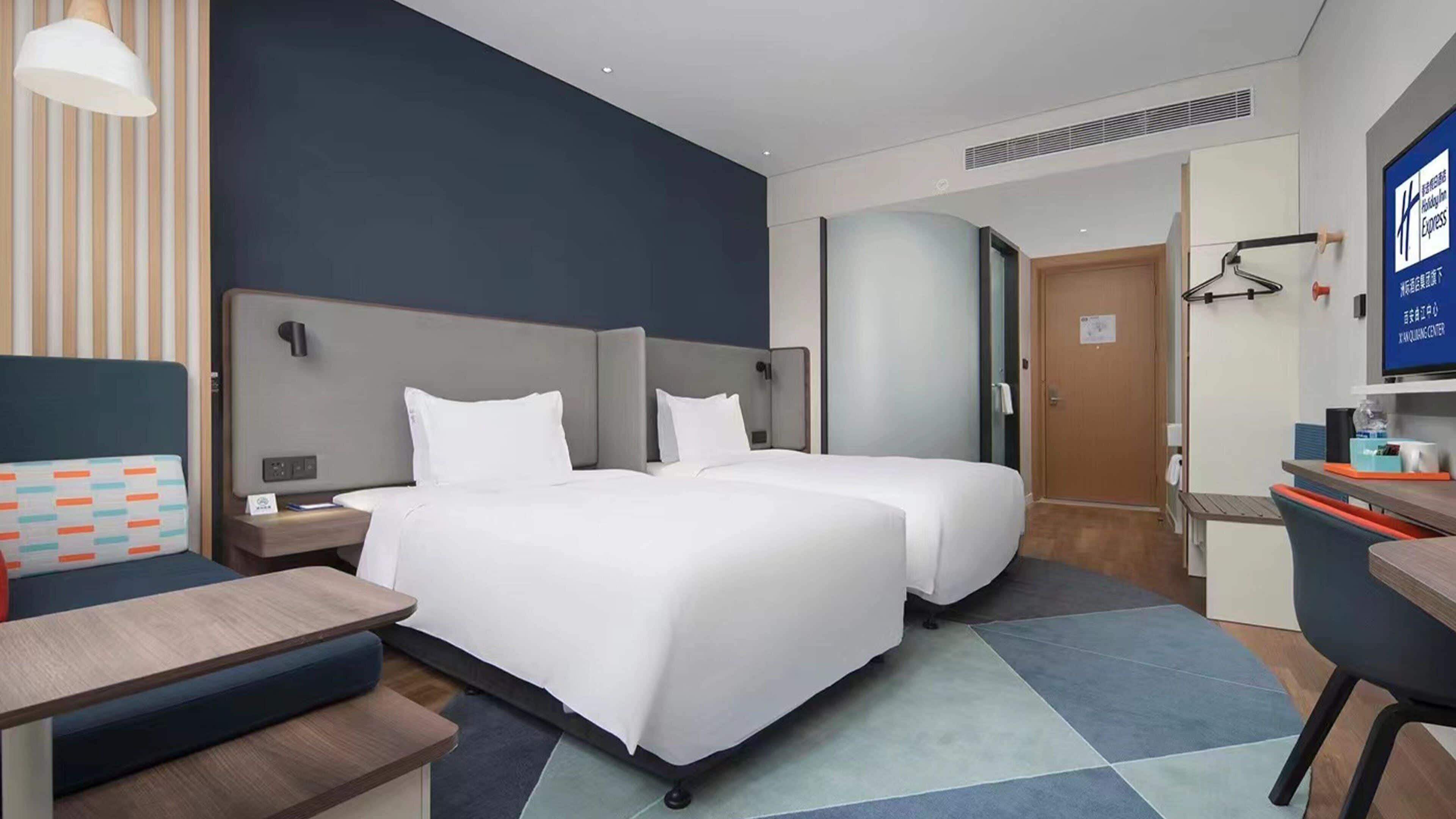 A hotel room with two beds, a desk, a chair, a television, and a bathroom door.