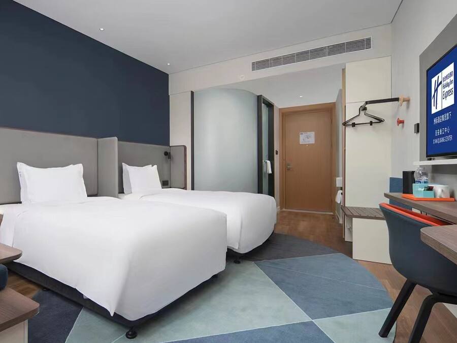 A hotel room with two beds, a desk, a chair, a television, and a bathroom door.