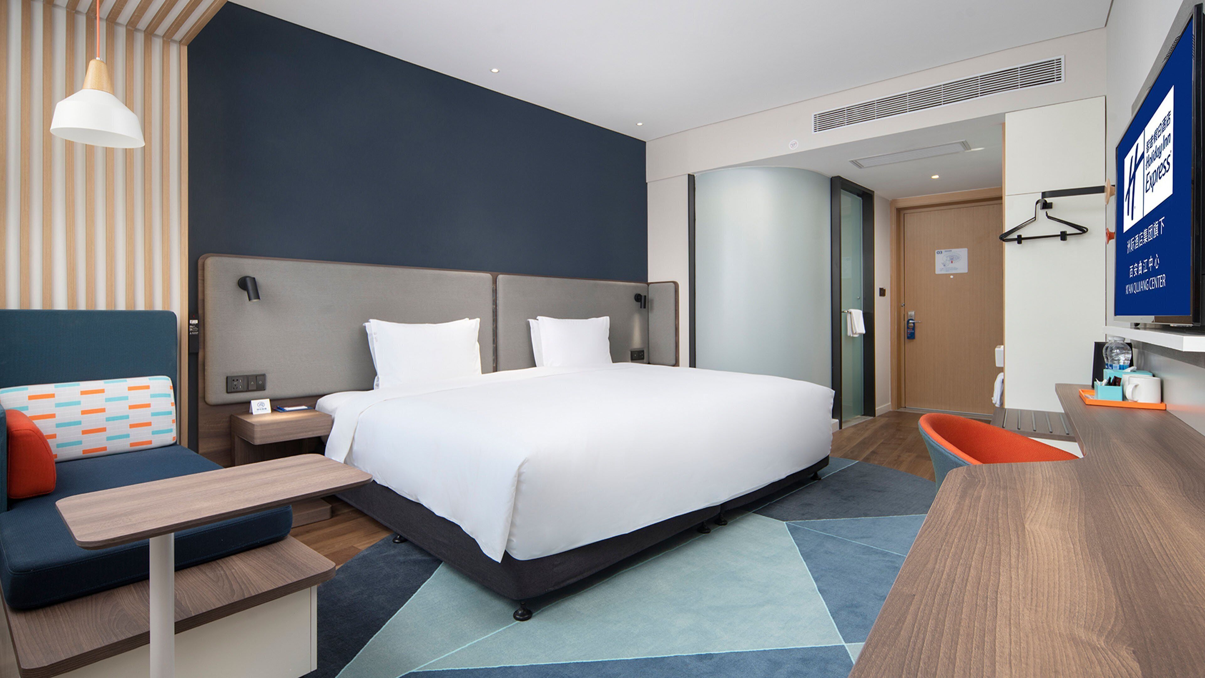Una habitación de hotel moderna con una cama grande, un escritorio, una silla y un televisor.
