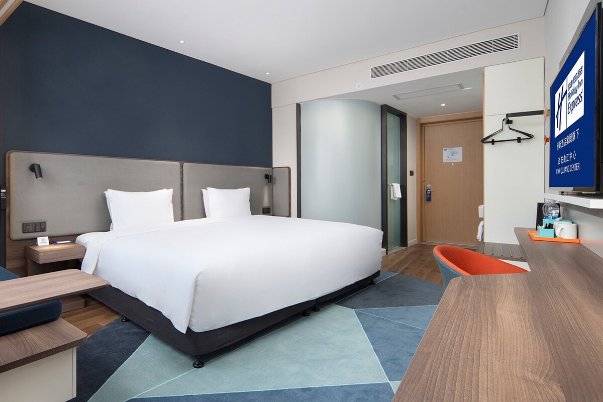 A modern hotel room with a large bed, a desk, a chair, and a TV.