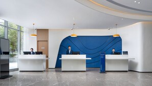 A modern reception area with two receptionists, a blue accent wall, and a clean, polished floor. - Holiday Inn Express Xian Quijang Center by IHG (Xi'an)