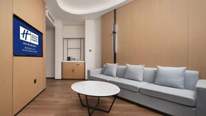 A modern hotel room with a sofa, a round table, and a kitchenette in the background. - Holiday Inn Express Xian Quijang Center by IHG (Xi'an)