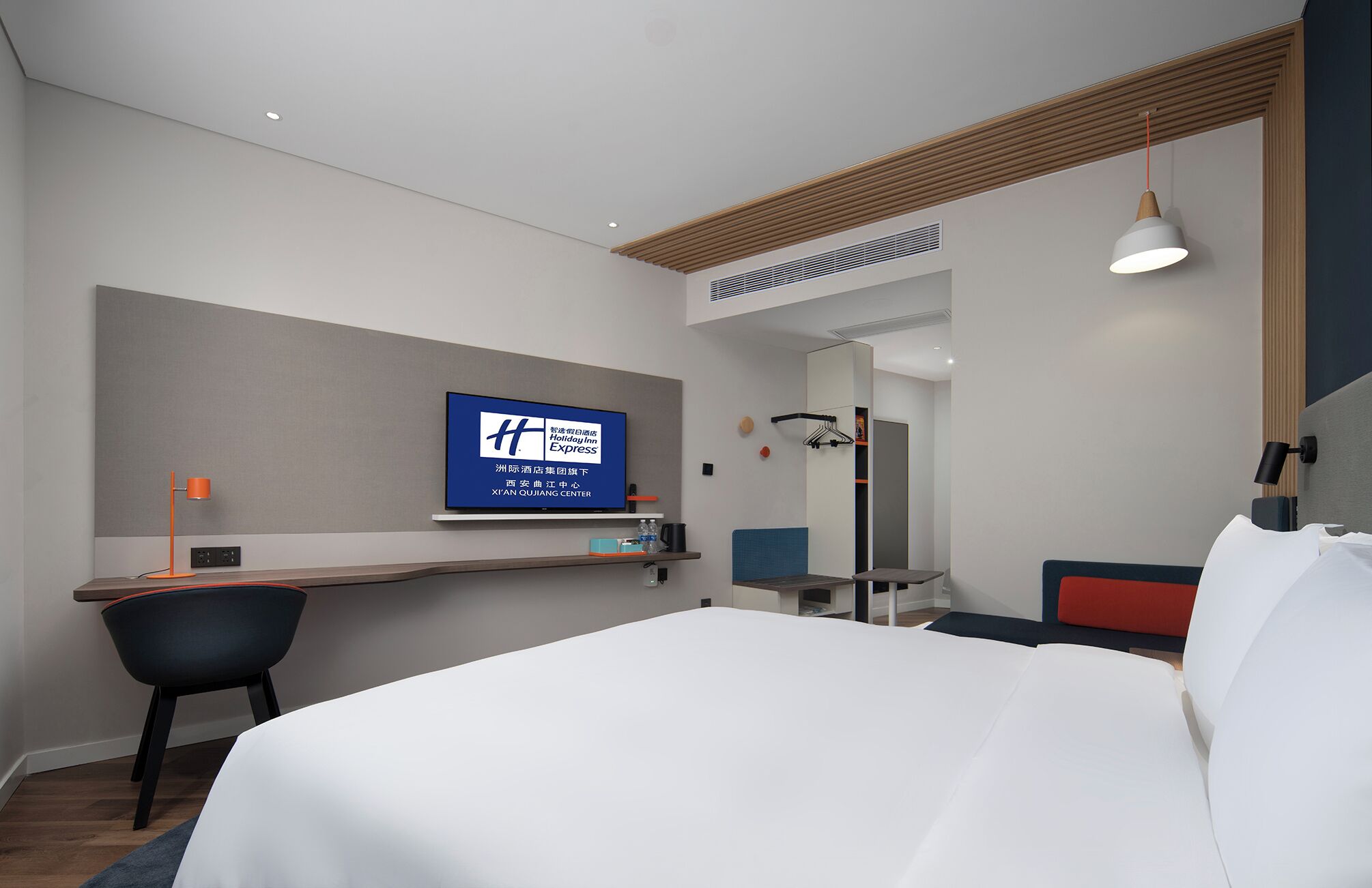 A hotel room with a bed, desk, chair, and a television displaying the Holiday Inn Express logo.