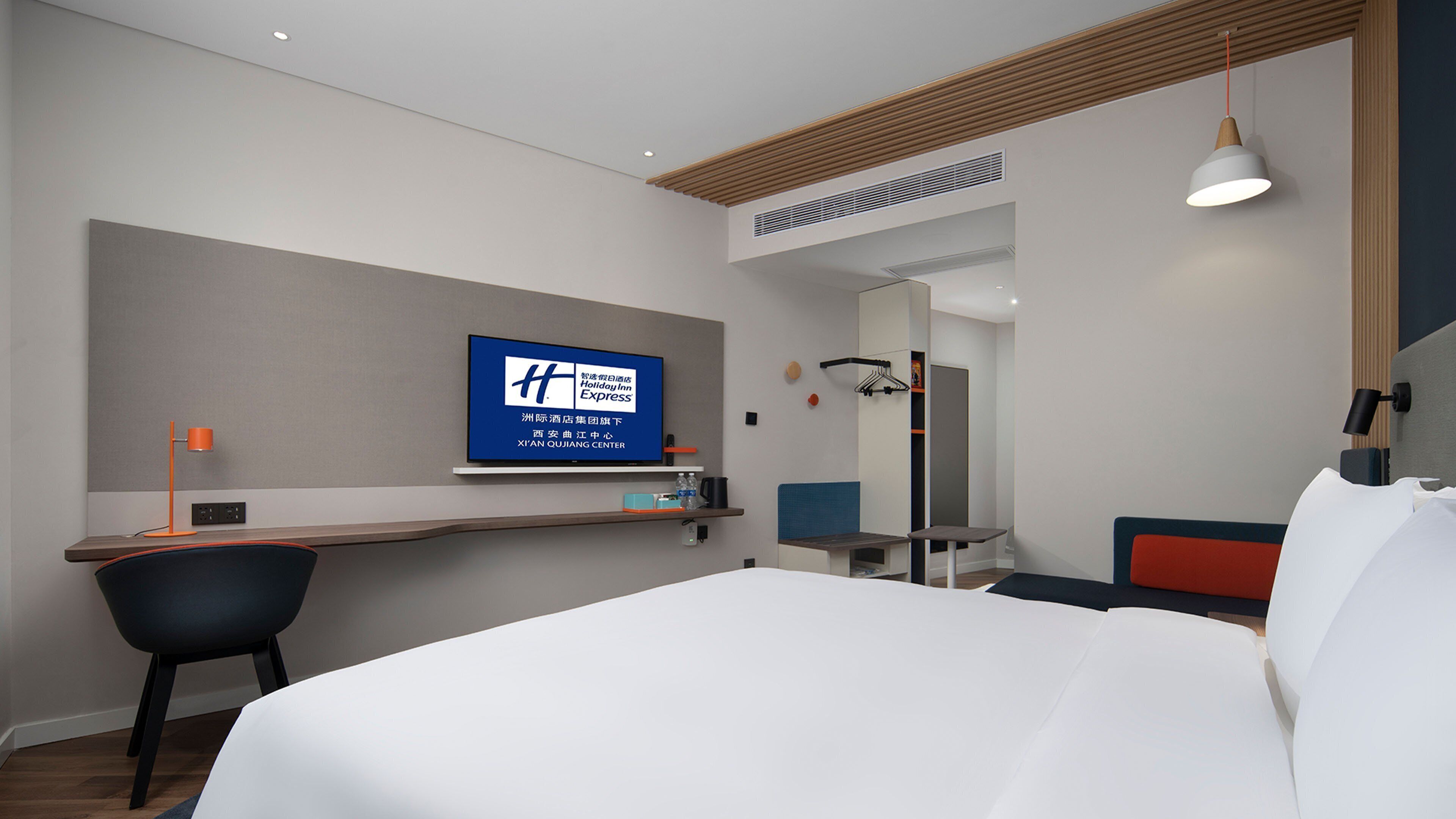 Une chambre d’hôtel moderne dotée d’un grand lit, d’un bureau avec un ordinateur, d’un téléviseur fixé au mur et d’un miroir au-dessus du bureau.