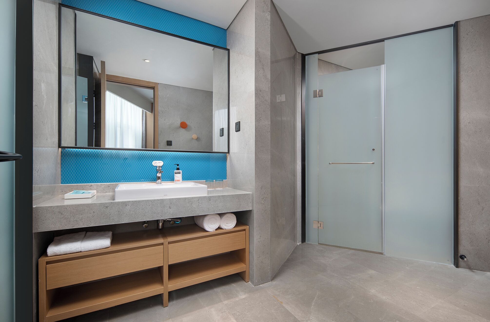 A modern bathroom with a large mirror, a white sink, and a wooden vanity.