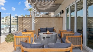 An outdoor seating area with wicker furniture and a central fire feature. - Persian Palms by RedAwning (St. George)