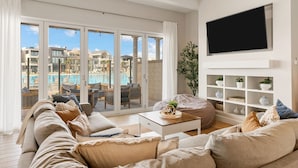 A living room with a sofa, a coffee table, and a TV. There is a balcony with a pool view. - Persian Palms by RedAwning (St. George)