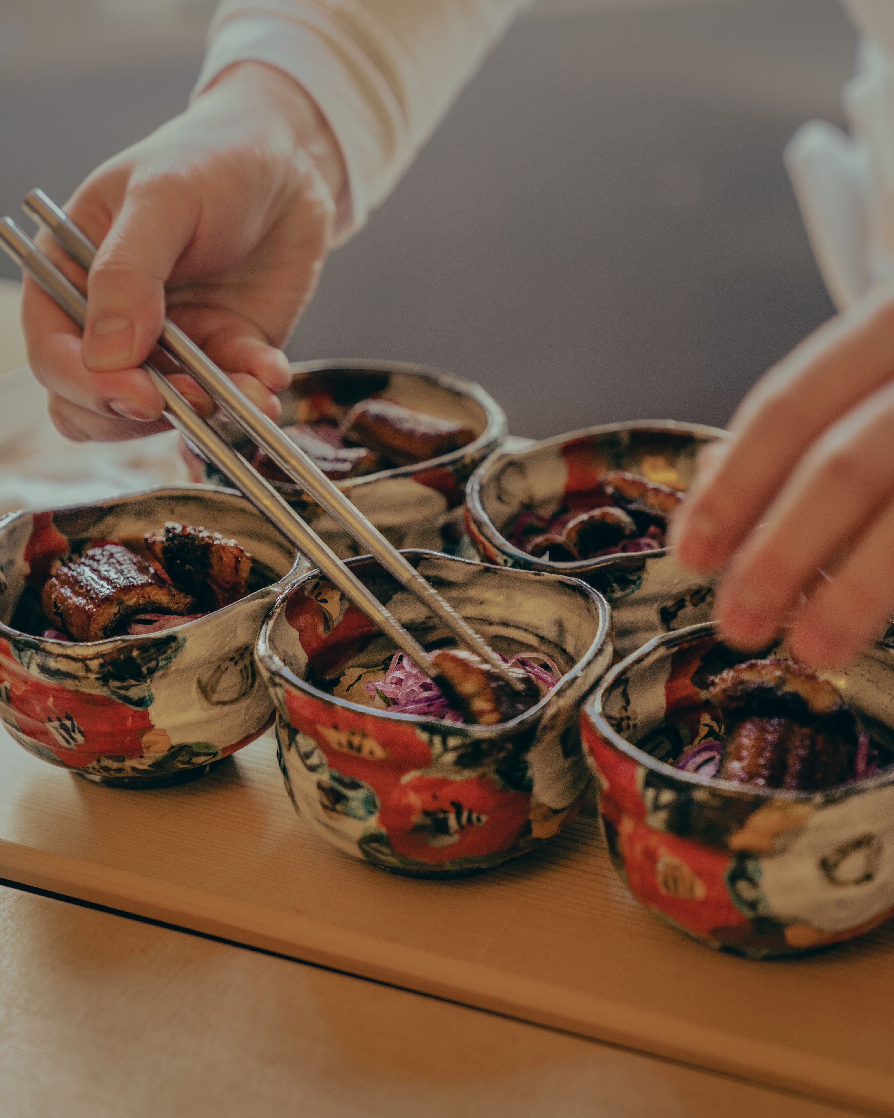 A person using chopsticks to eat from a bowl with a floral pattern.