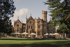 A large, historic building with multiple towers and a well-maintained lawn in front.