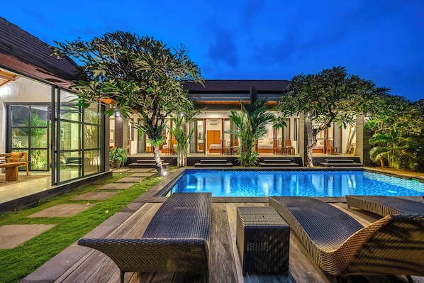 A modern pool area with lounge chairs, a swimming pool, and a well-maintained garden.