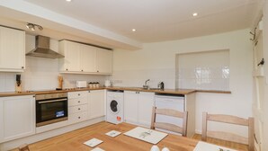 A modern kitchen with white cabinets, a wooden countertop, a built-in oven, a washing machine, and a dining table with placemats and eggs. - 2 Court Farm (Wareham)