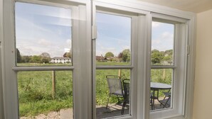 A room with a large window overlooking a grassy area and a chair. - 2 Court Farm (Wareham)