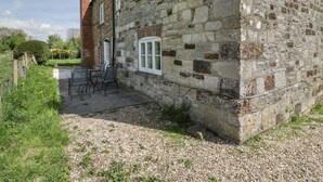 A stone building with a gravel path leading to a seating area with chairs and a table. - 2 Court Farm (Wareham)
