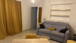 A modern living room with a grey sofa, yellow chairs, a wooden dining table, and a clear glass coffee table. - Gîte des oliviers (Vénéjan)
