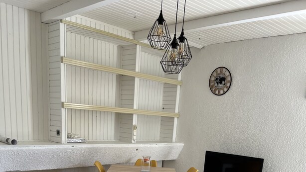 A modern living room with a dining area, a TV, and a kitchen counter. - Gîte des oliviers (Vénéjan)