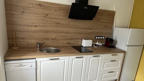 A kitchen with a wooden countertop, a sink, a dishwasher, a black range hood, and a white refrigerator. - Gîte des oliviers (Vénéjan)
