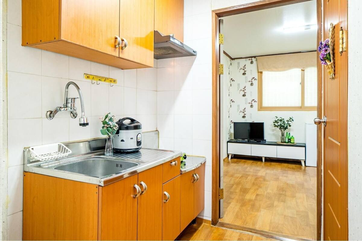 A compact kitchen with wooden cabinets, a stainless steel sink, a kettle, and a small countertop.