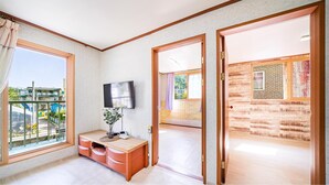 A modern room with a TV, wooden furniture, and a balcony with a view. - Gangchon Pine Hill Pension (Chuncheon)