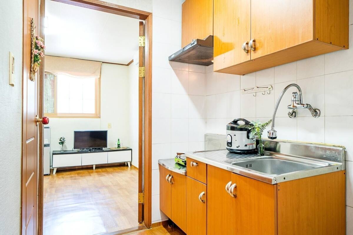 A compact kitchen with wooden cabinets, a stainless steel sink, and a built-in range hood.