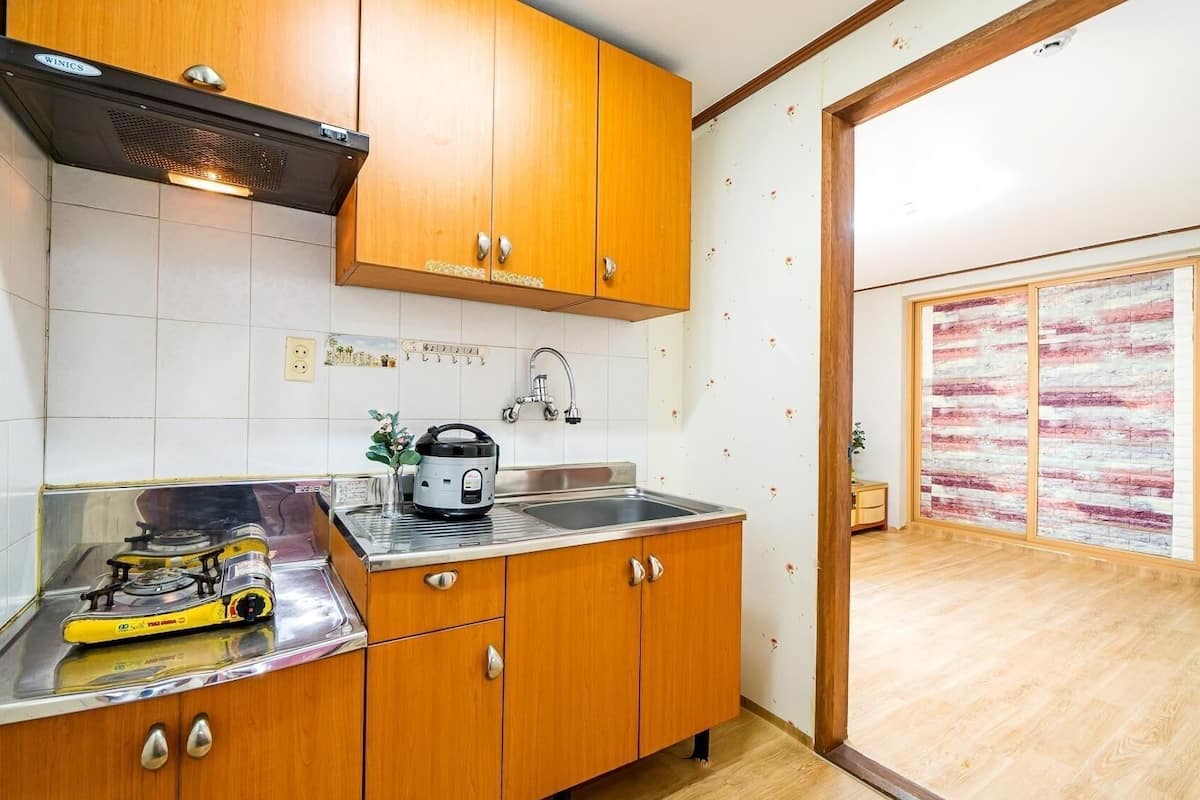 A compact kitchen with wooden cabinets, a gas stove, a sink, and a kettle.