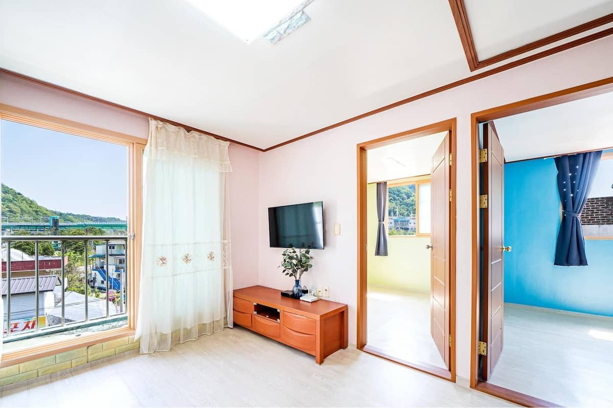A room with a large window, a TV, a wooden cabinet, and a sliding door leading to an outdoor area.