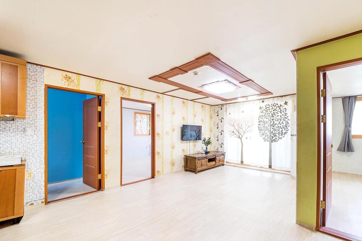 A spacious room with a wooden cabinet, a blue door, a television, and a decorative tree on the wall.