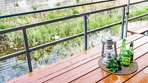 A wooden deck with a metal railing overlooking a grassy area and a body of water. - Gangchon Pine Hill Pension (Chuncheon)