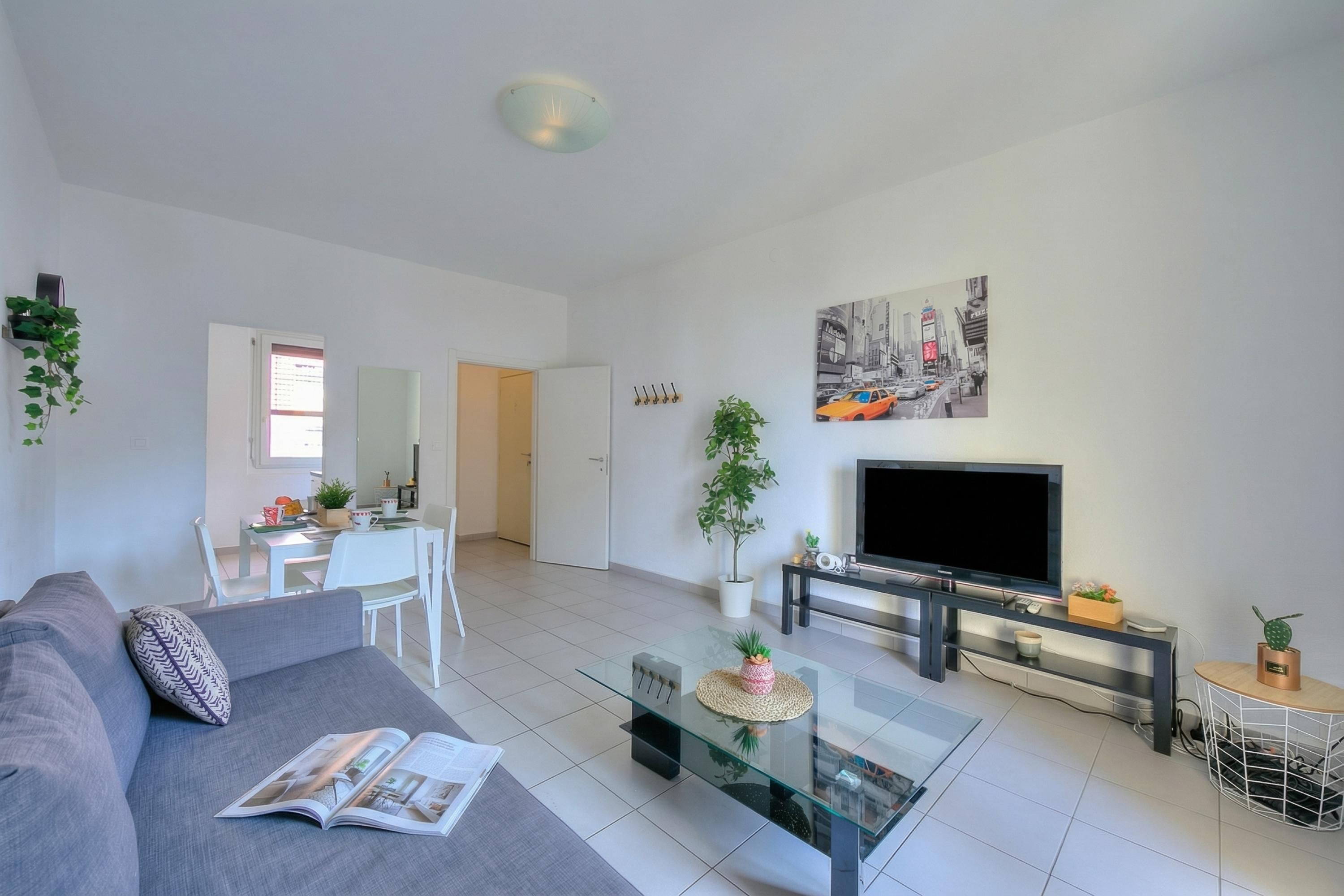 A modern living room with a sofa, coffee table, TV, and dining area.