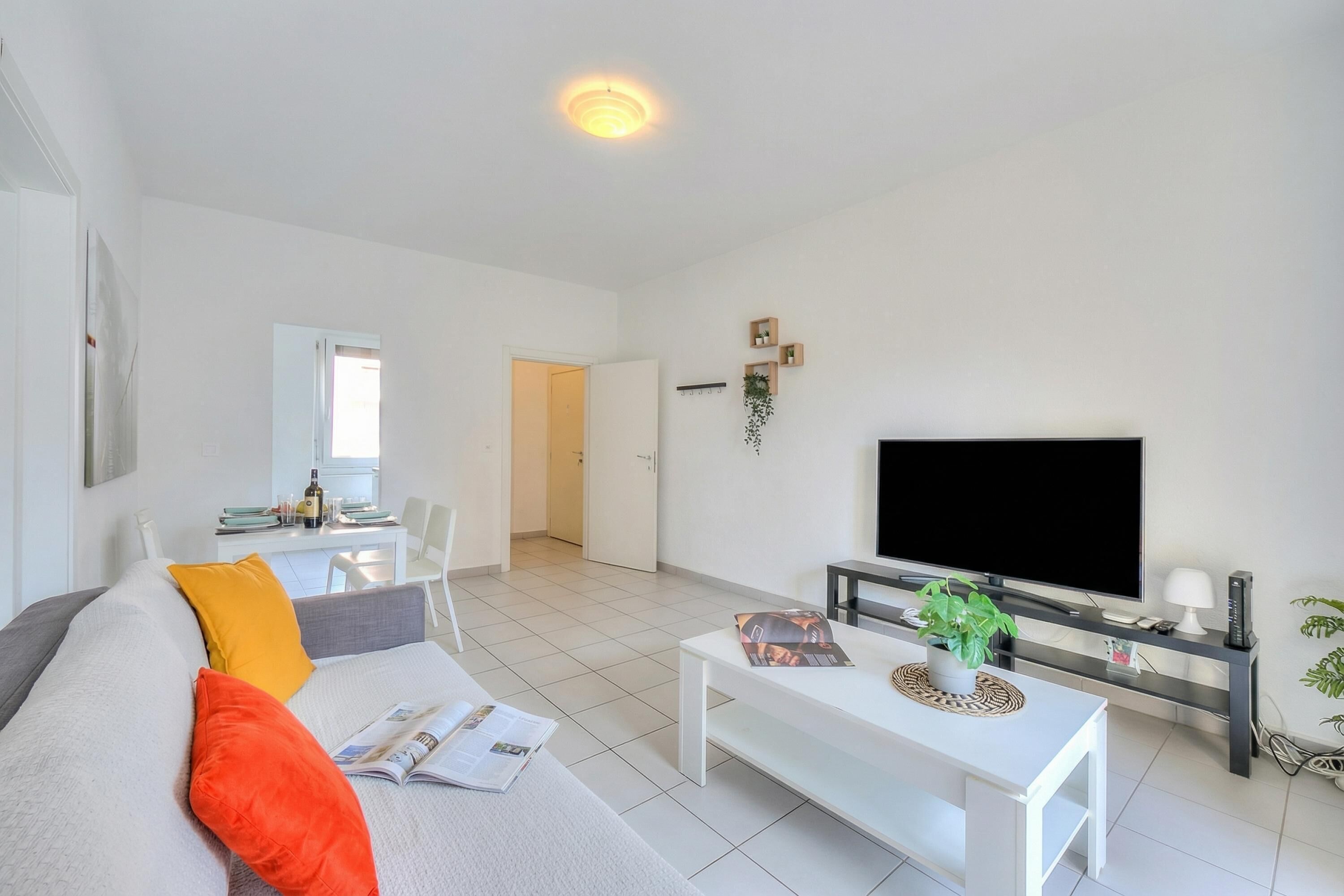 A modern living room with a sofa, coffee table, TV, and a dining area with chairs and a table.