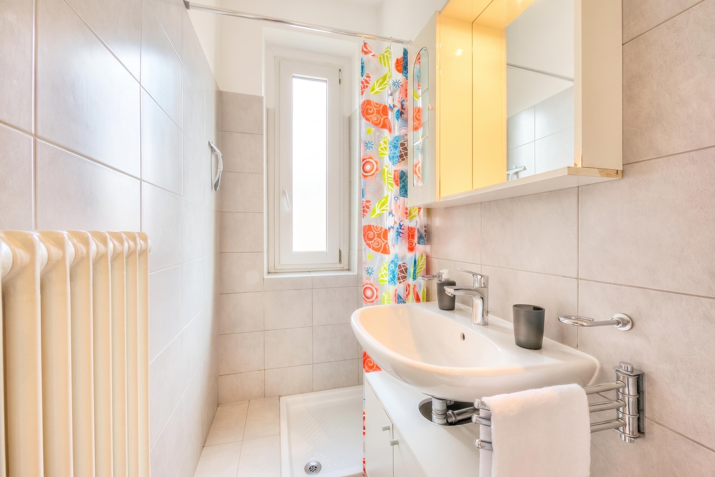 A modern bathroom with a white sink, a mirror, a shower, and a colorful shower curtain.