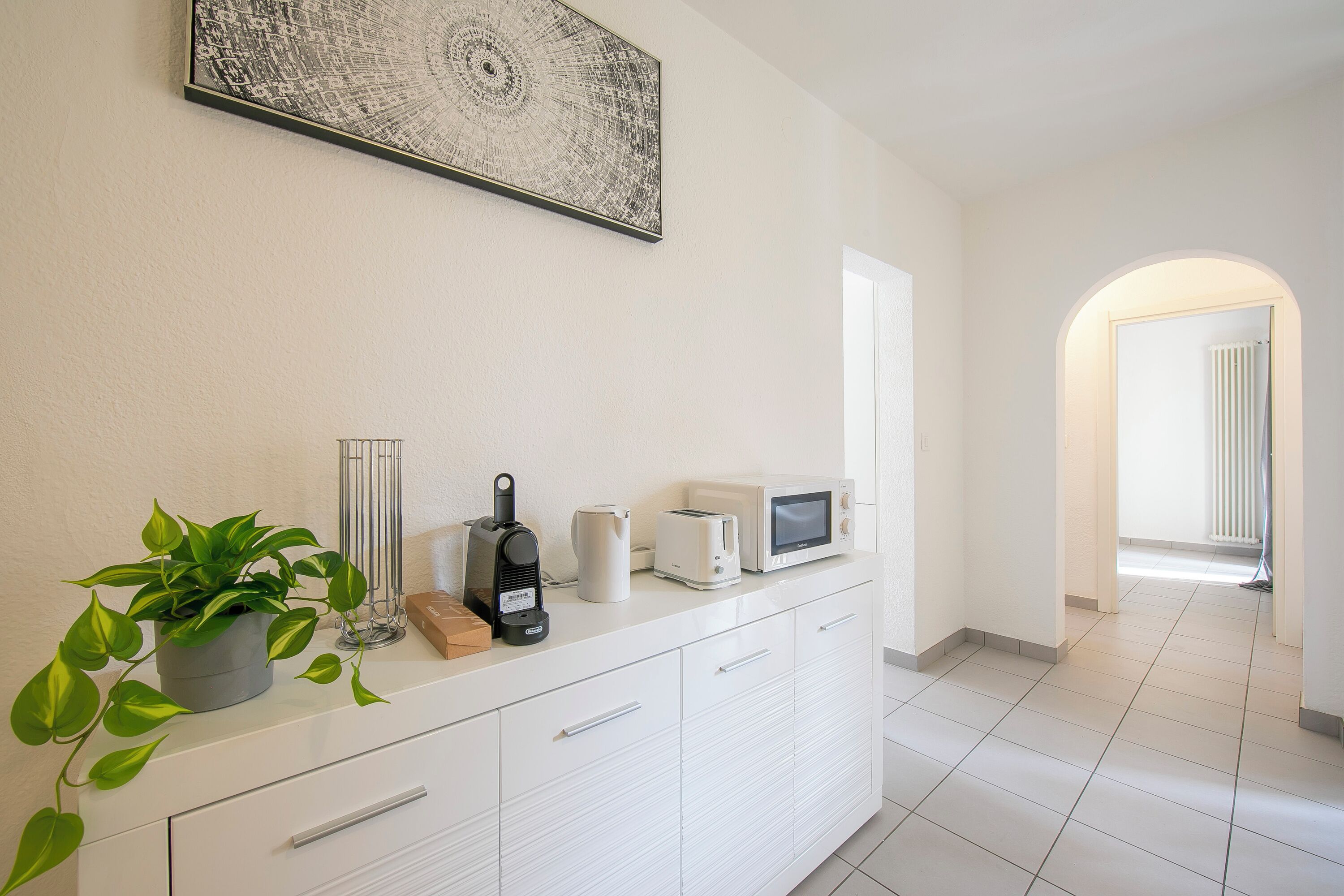A modern kitchen with a white countertop, a potted plant, a coffee maker, a toaster, and a microwave.