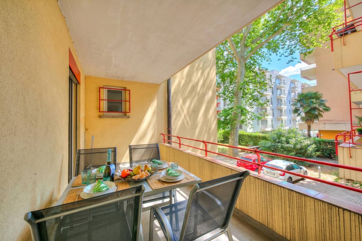 Un balcón con una mesa de comedor para dos personas, sillas y barandilla roja.