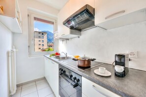 A modern kitchen with a stove, oven, sink, and a window with a view of buildings and mountains.