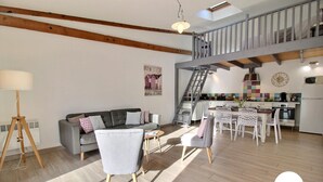 Ein großzügiger Wohnbereich mit Sofa, Esstisch und Stühlen, eine Treppe zu einer oberen Ebene sowie eine Küchenzeile mit modernen Geräten.