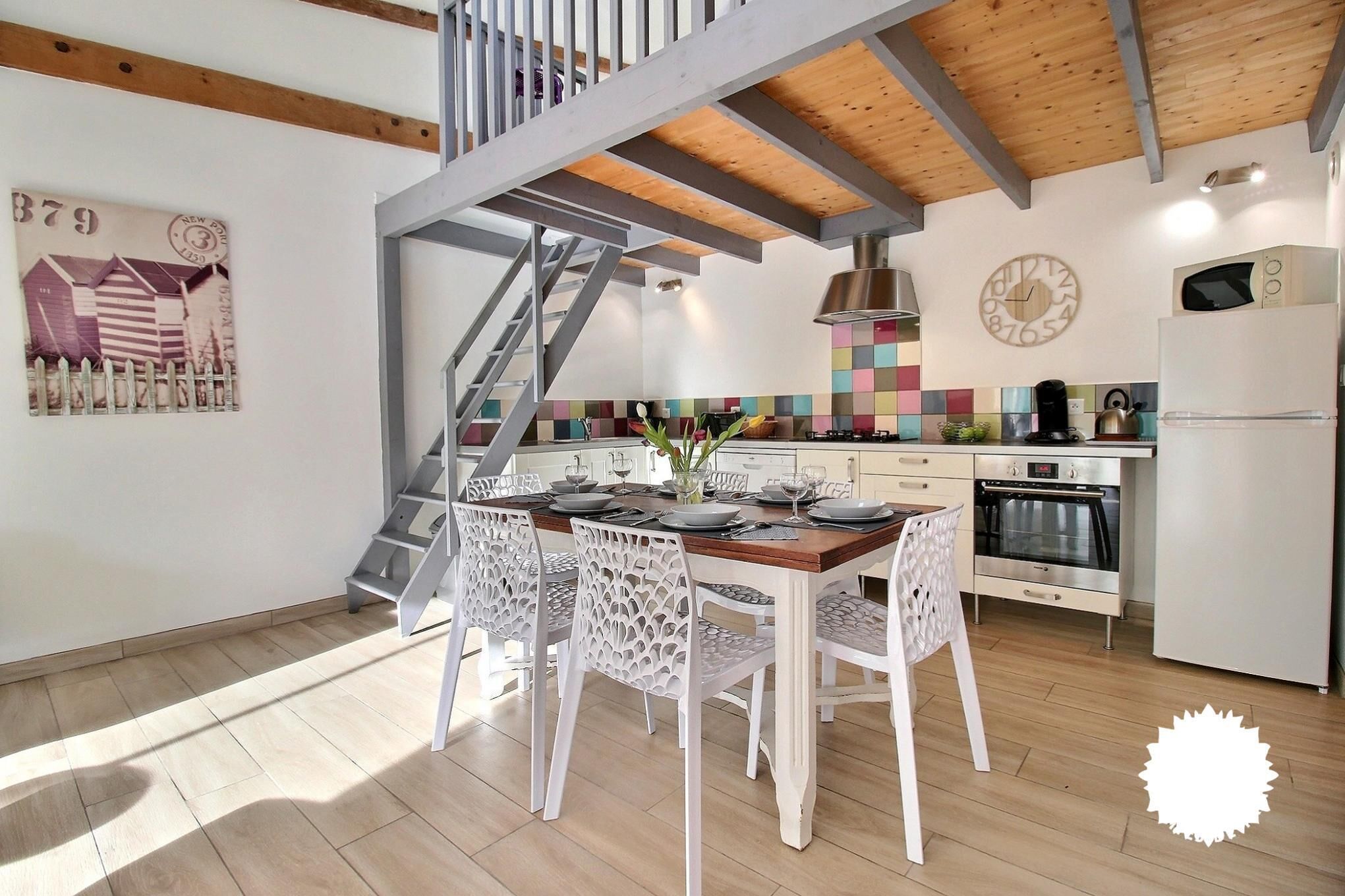 Een moderne keuken met een houten plafond, een trap en een eethoek met witte stoelen.