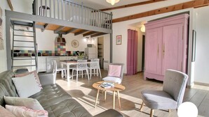 Ein modernes Wohnzimmer mit Sofa, Sessel und Couchtisch. Im Hintergrund ist eine Küche mit Essbereich erkennbar.