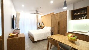 A hotel room with a bed, a desk, a chair, a small table with fruit, a mirror, and a window with curtains. - Oriana Hotel 2 (Hanoi)