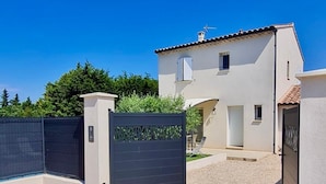 Uma casa moderna de dois andares, com entrada por um caminho de cascalho e um portão preto.