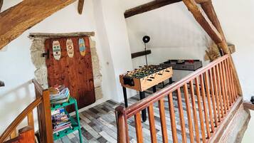 Eine rustikale Holztreppe mit einer Holzhandläufe, die zu einem Raum führt, in dem ein Tischfußballtisch und ein Bücherregal zu sehen sind.