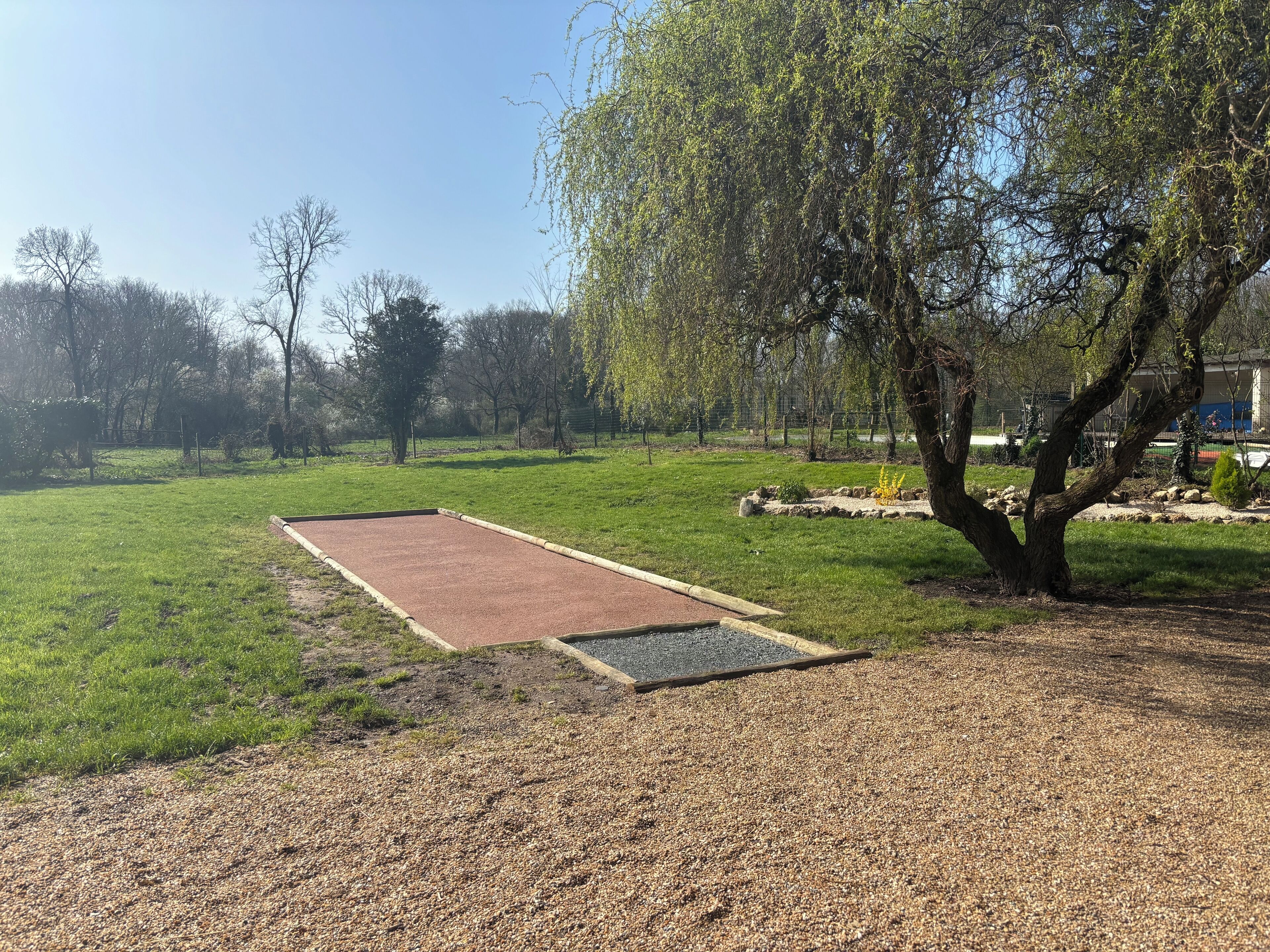 Una zona de grava con superficie roja de caucho, rodeada de césped y árboles.