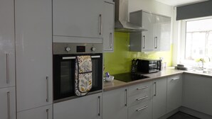 A modern kitchen with grey cabinets, a built-in oven, a microwave, and a window with a view. - Lady Wilson Apartment (Airdrie)