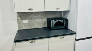 A compact kitchen with white cabinets, a black countertop, and a microwave. - Lady Wilson Apartment (Airdrie)
