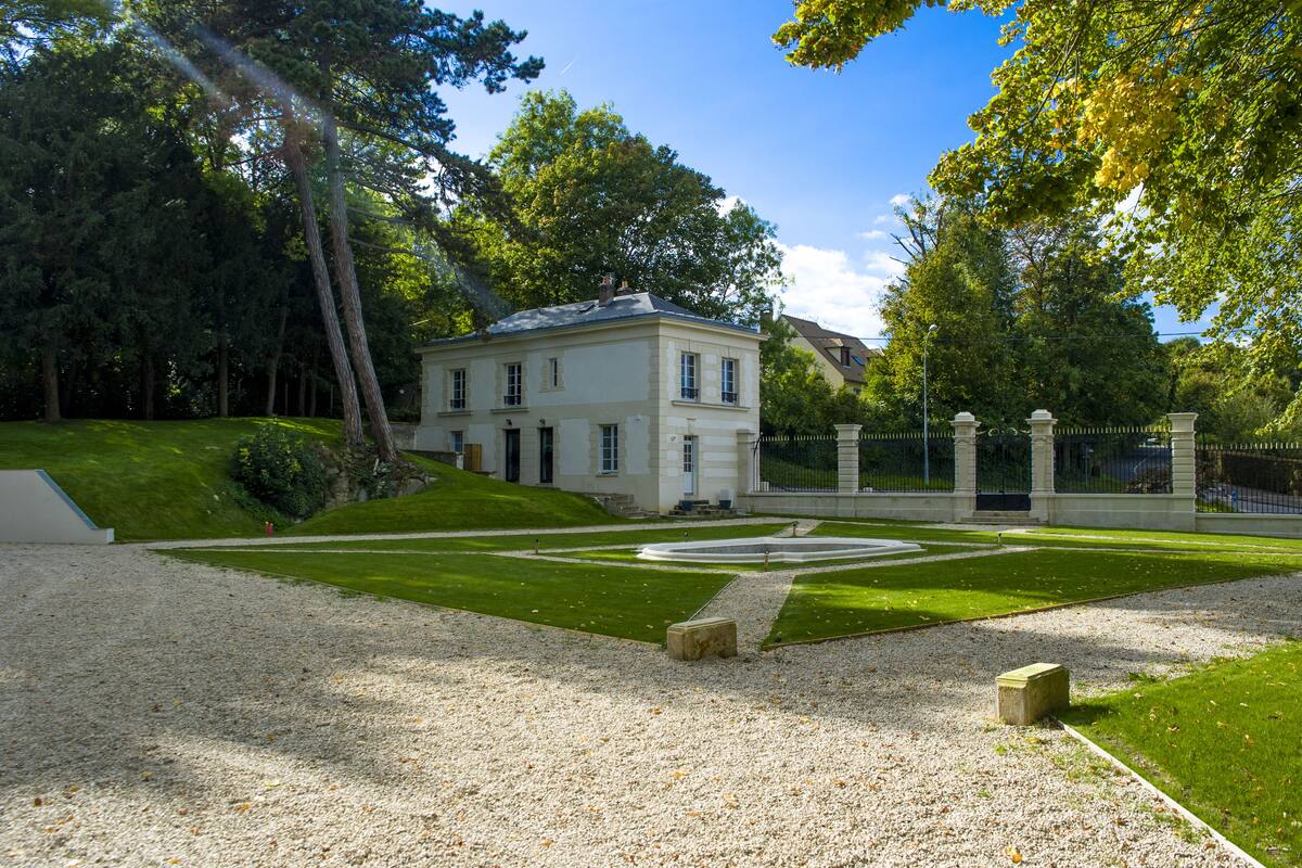 A historic building with a symmetrical lawn and a gravel path leading to the entrance.
