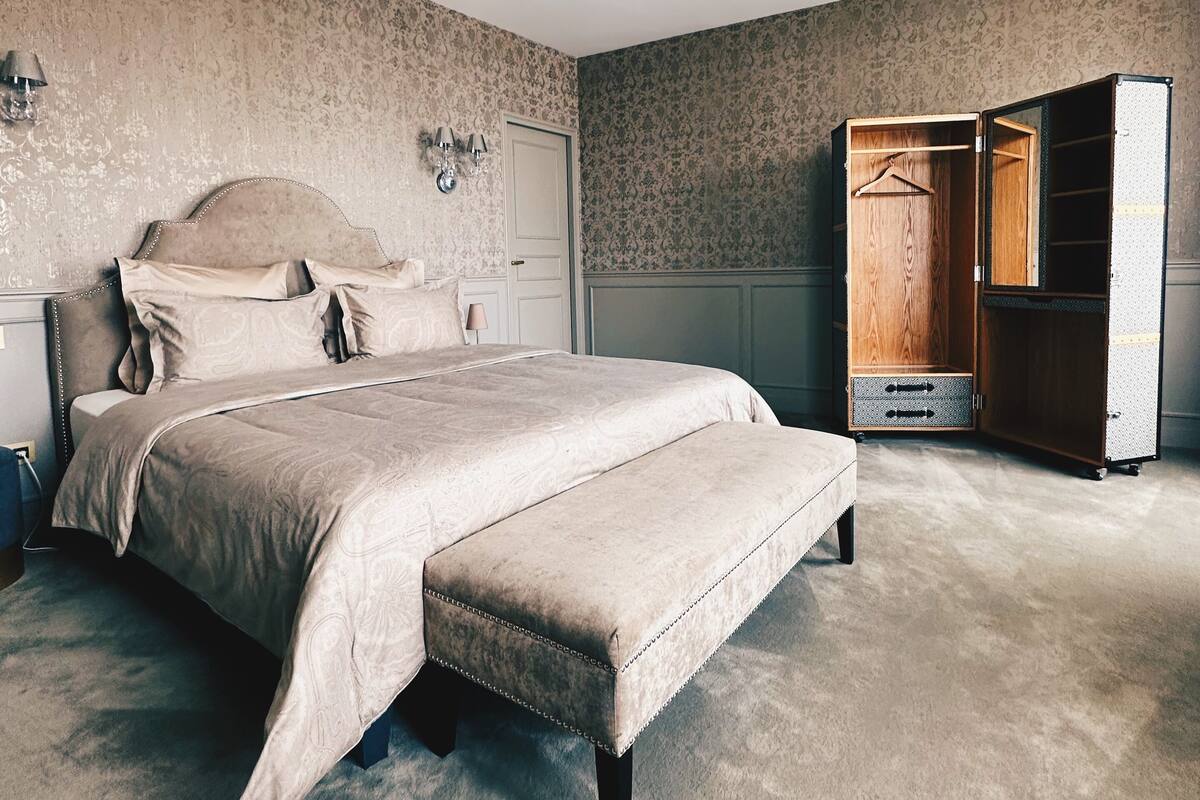 A bedroom with a large bed, a bench, a wardrobe, and a dresser.