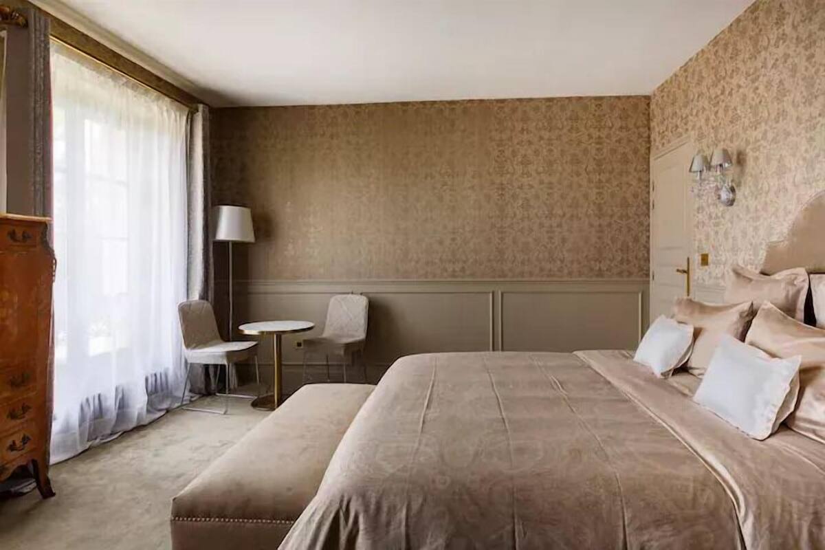 A hotel room with a large bed, a small table, two chairs, and a wardrobe.