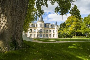 Ein großes, historisches Gebäude mit einem zentralen Turm und mehreren Flügeln, umgeben von einem gepflegten Rasen und Bäumen.