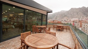 Une terrasse avec des tables et des chaises en bois, un mur de verre et une vue sur le paysage urbain et les montagnes.