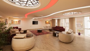 Un salon spacieux, doté de meubles modernes, d’une grande fenêtre et d’un plafond au design original.
