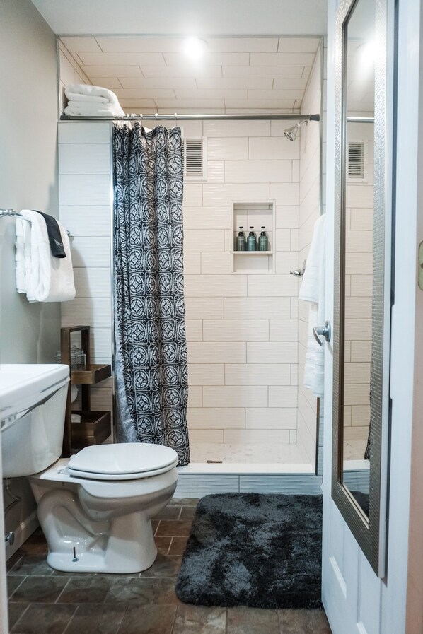 Une salle de bain comprenant des toilettes, une douche avec un rideau à motifs, un lavabo et un miroir.